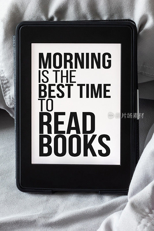 现代的电子阅读器，在灰色和紫色的床上，屏幕上显示着文字——早上是阅读书籍的最佳时间。Tablet with a quote about reading on microfiber寝具特写